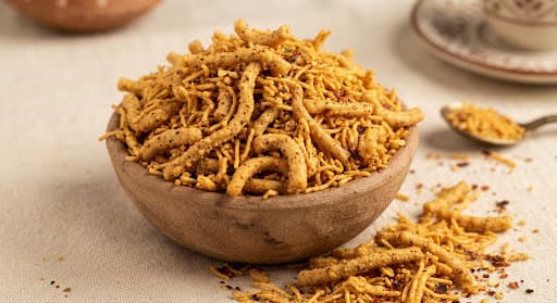 Golden crispy Ratlami sev and Rajasthani spicy bhujia overflowing from an earthenware katori